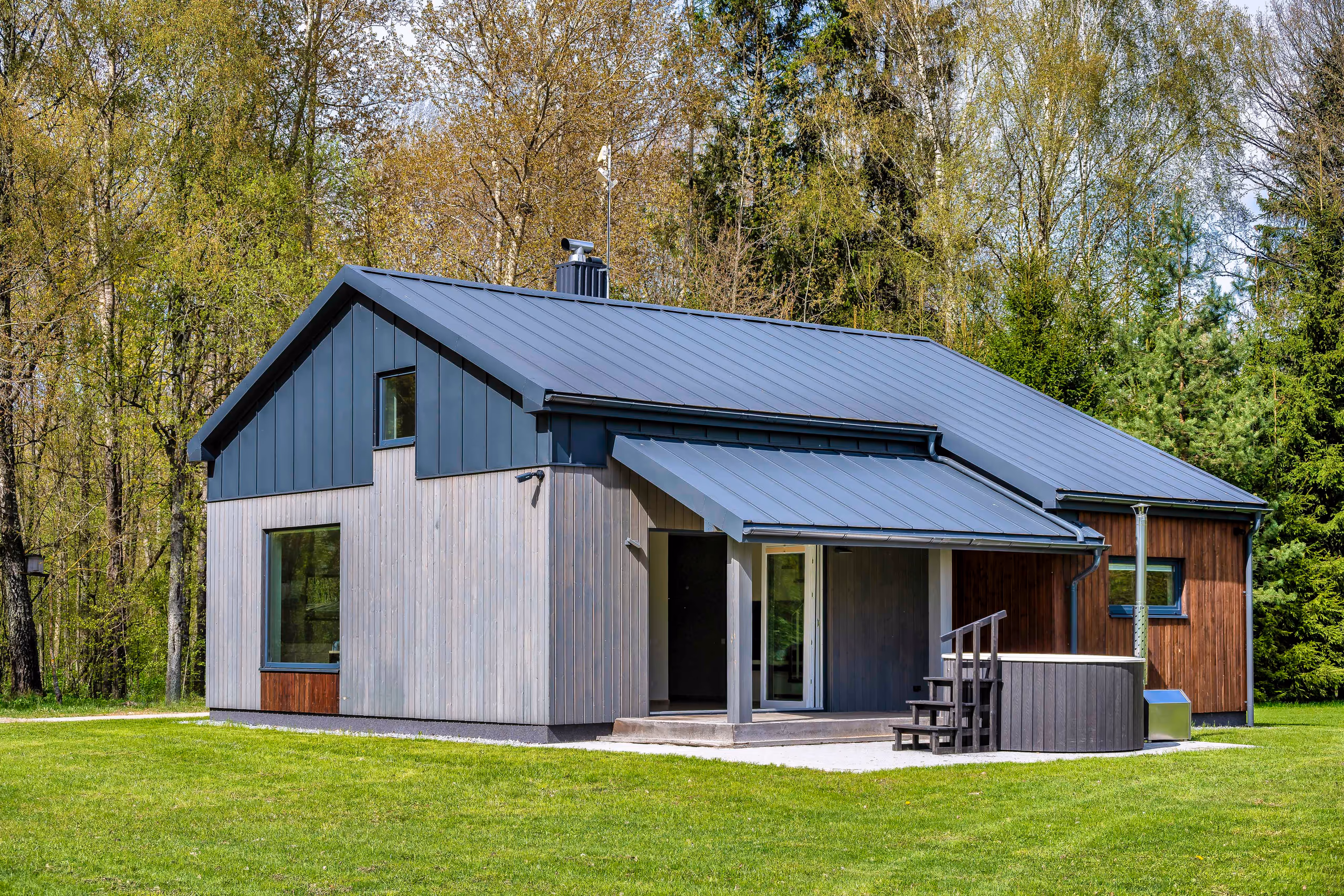 Vila Valentino cabin from the side with dark vertical wood cladding, black metal roof, hot tub and lawn