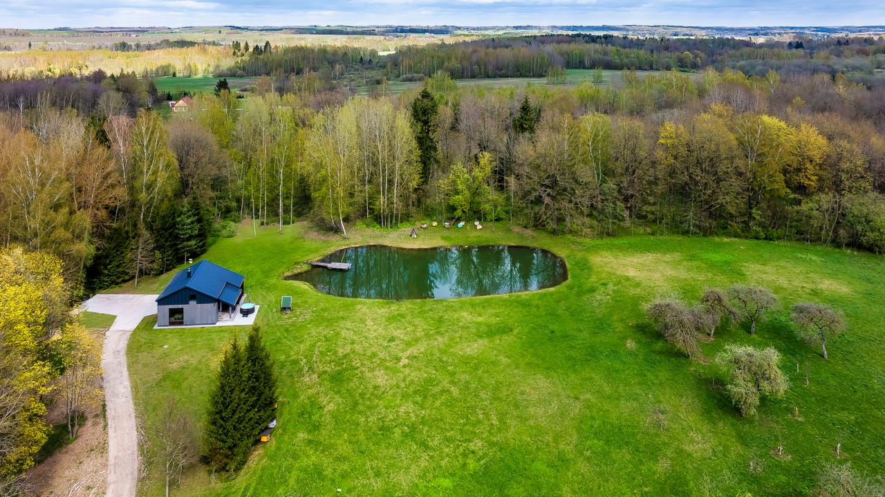 Aerial of Vila Valentino in spring with black cabin, private pond and rolling Ukmergė fields beyond