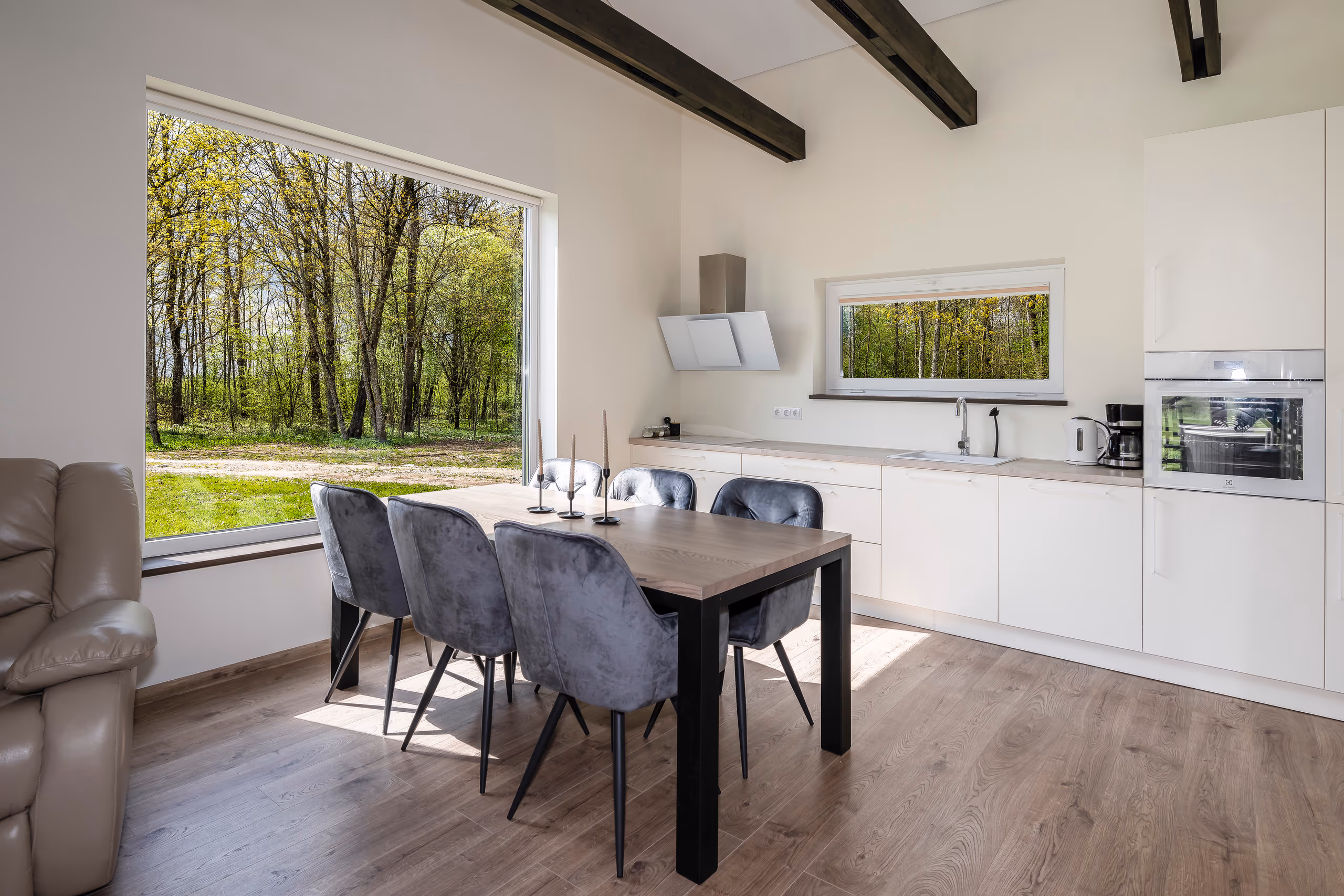 Vila Valentino white kitchen and dining with dark ceiling beams and a tall window onto the forest
